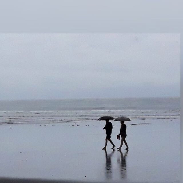 Pareja paseando por la playa bajo la lluvia